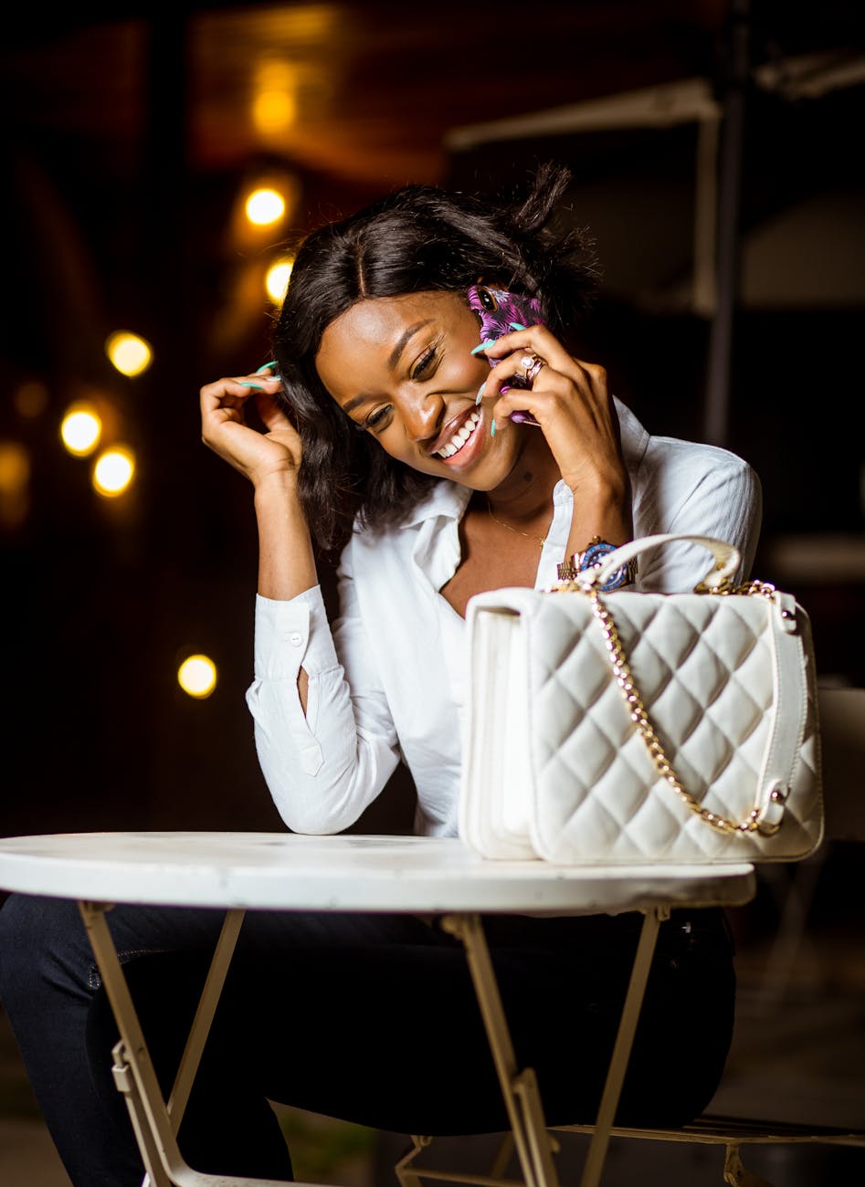 woman in white top and black pants sitting holding a cellphone